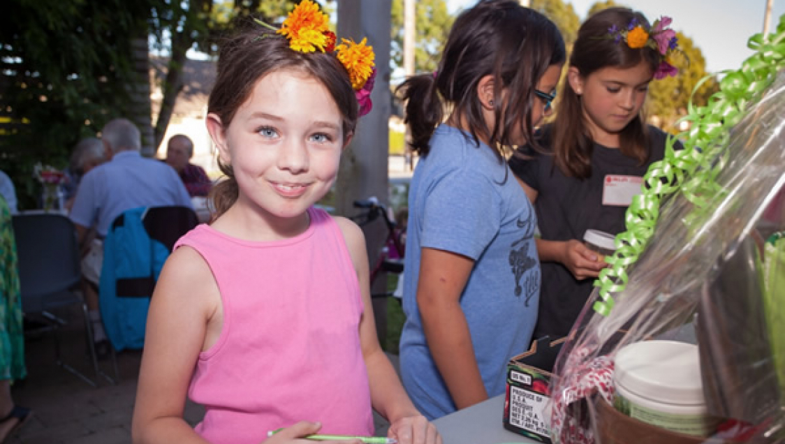 Children with flowers in their hair. Other community members are in the background.