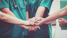 Nurses standing in a circle with hands clasped.