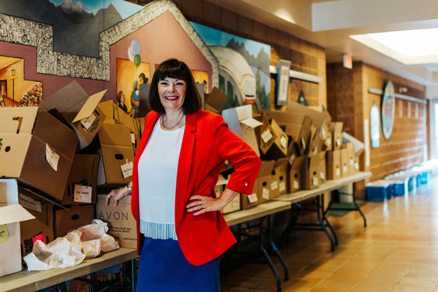 A woman standing before a length of folding tables covered in stacked cardboard boxes and smiling