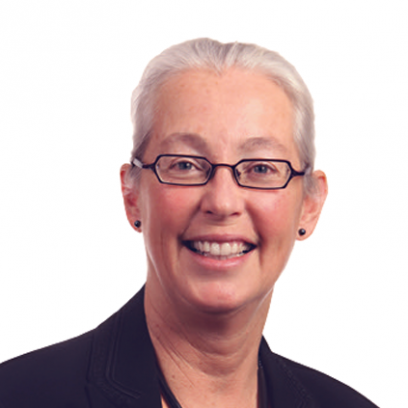 Headshot of Brenda Eaton, a smiling woman with light eyes and white hair wearing glasses and a dark purple blazer