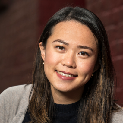 Headshot of Camille Wong, a smiling woman with long dark hair, brown eyes and dimples wearing a dark top and grey cardigan