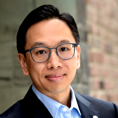 Headshot of Eugene Lee, a smiling man with short dark hair wearing square framed glasses and a dark suit with light blue shirt