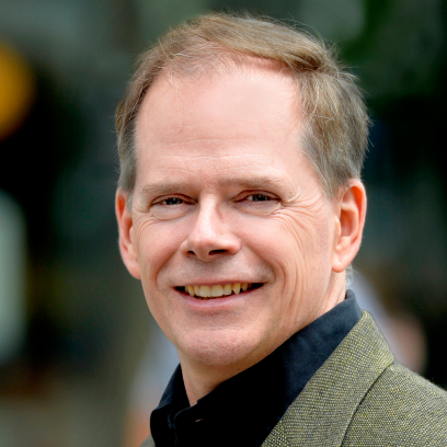 Headshot of Kevin McCort. He has sandy salt-and-pepper hair and is wearing a tan suit and dark shirt.