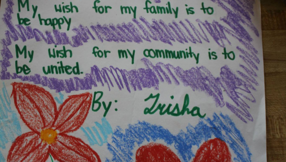 Child's crayon drawing of a flower with the words "My wish for my family is to be happy, my wish for my community is to be united"