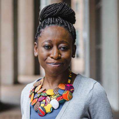 Headshot of Amora Takawira, a smiling woman with braided updo wearing a necklace of patterned and colourful circles