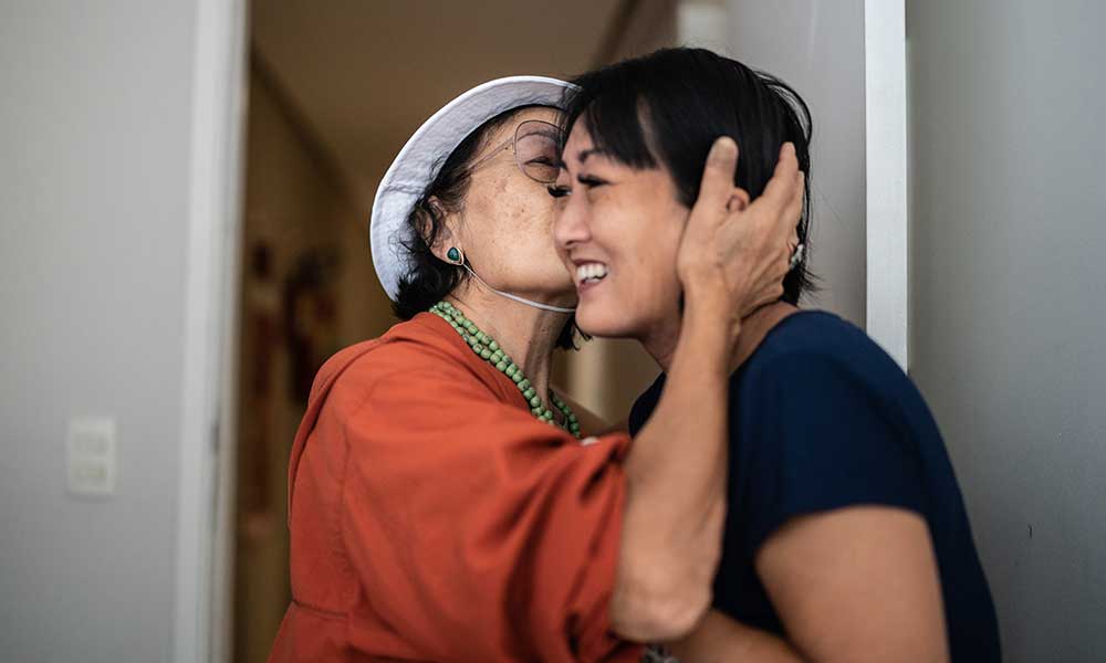 Asian mom kissing her daughter on the cheek upon coming home