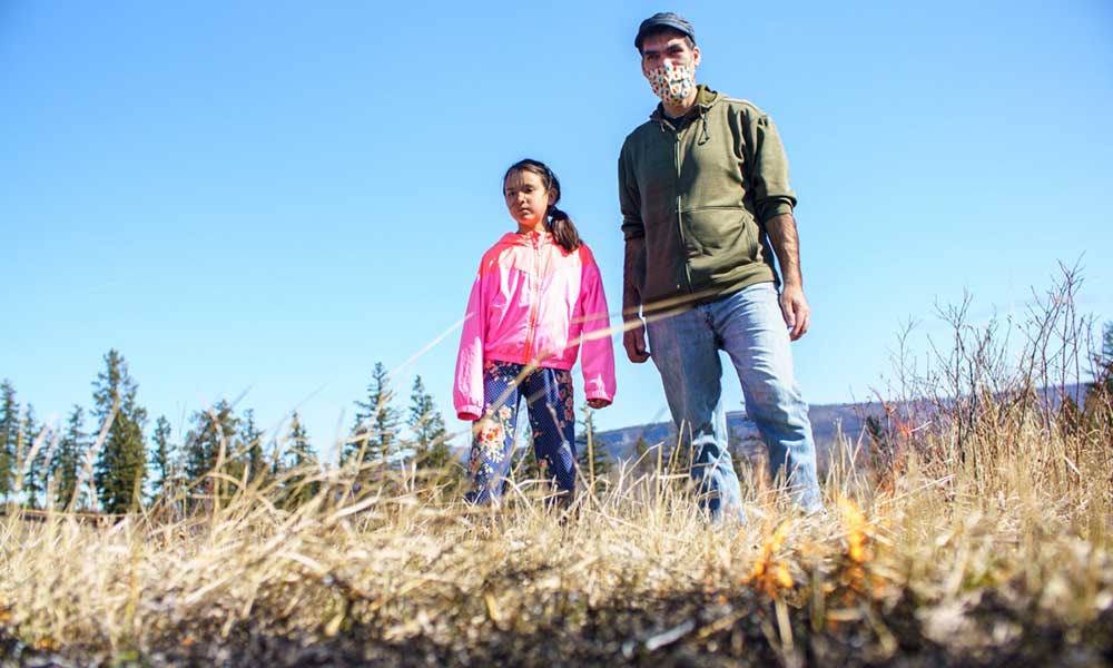 Man wearing a face-mask standing beside a young girl in a dry field