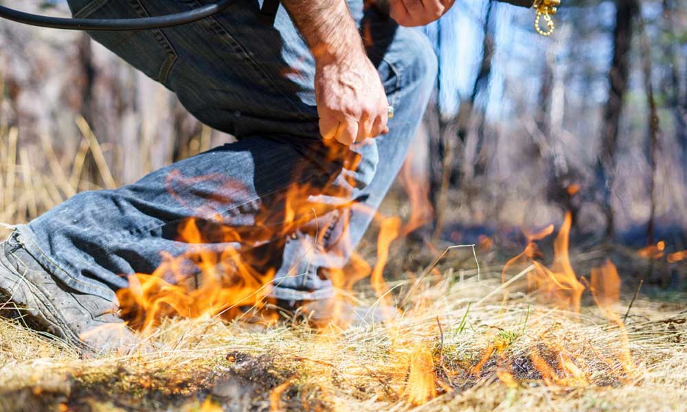 GVS6 Waist down shot of a man in jeans standing near dry brush that has caught fire