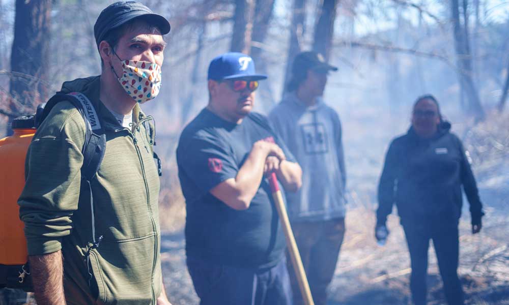 Four people standing in the smoky woods looking concerned