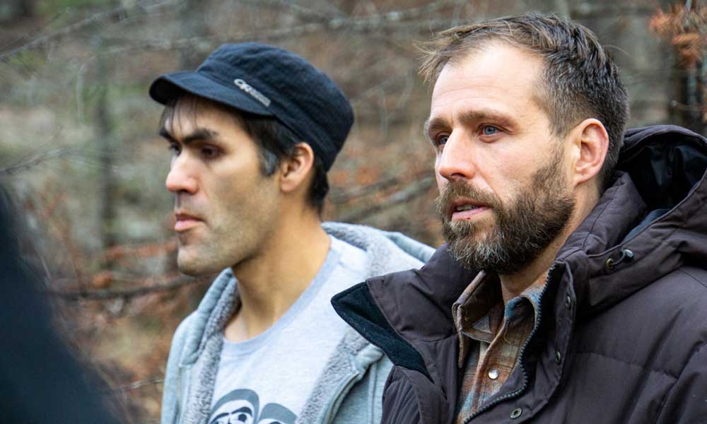 Close up of two men in the woods looking serious and concerned