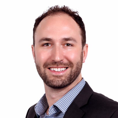Jon Sharun A smiling man with brown eyes, hair and beard wearing a checked shirt and dark brown jacket