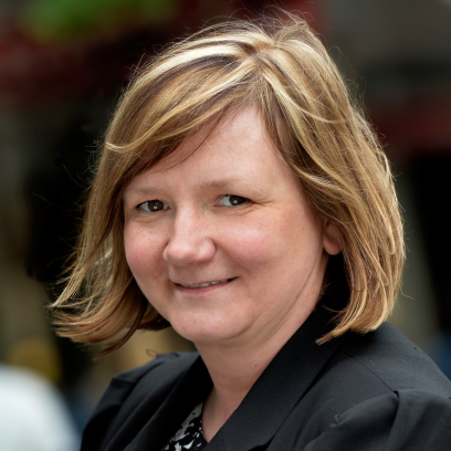 Headshot of Nicole Jeschelnik, a smiling woman with short blonde hair and brown eyes wearing a dark blouse and jacket