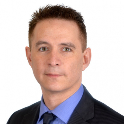 Headshot of Paul Lacerte. He has short brown hair and hazel eyes, and is wearing a blue shirt and a dark suit and tie.