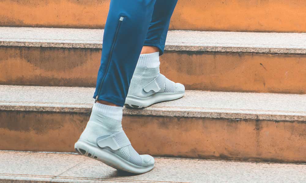 Person wearing jeans and street shoes takes the first step up a flight of stairs.