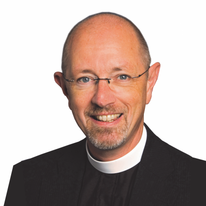 Headshot of Peter Elliott. He has light eyes and wire-rimmed glasses, and is wearing a dark shirt and jacket with a white clerical collar around the neck.