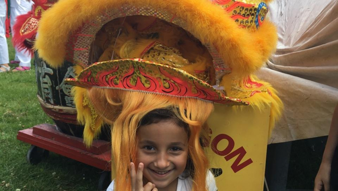 A smiling dark haired child wearing the head-dress part of a chinese Dragon costume