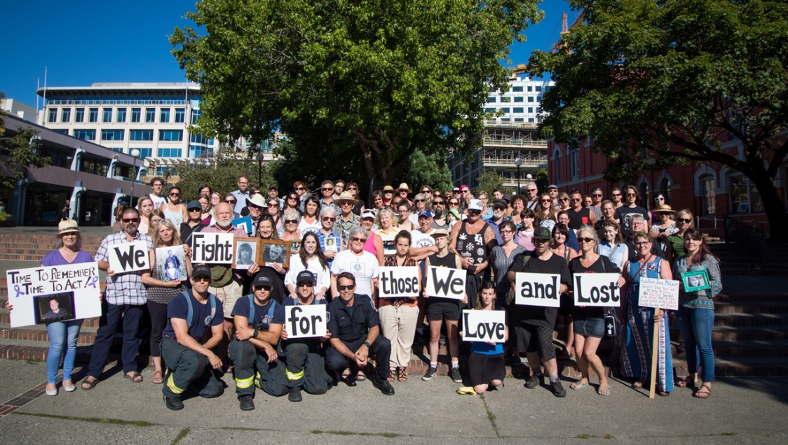 A group of people standing together, holding pictures of loved ones and signs that read "We fight for those we love and lost" for Overdose Awareness Day 2017.