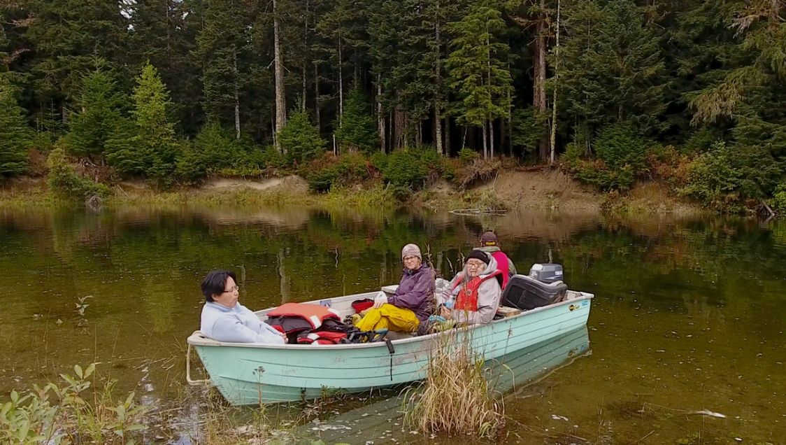 Four people in a small mint green rowboat near the shoreline