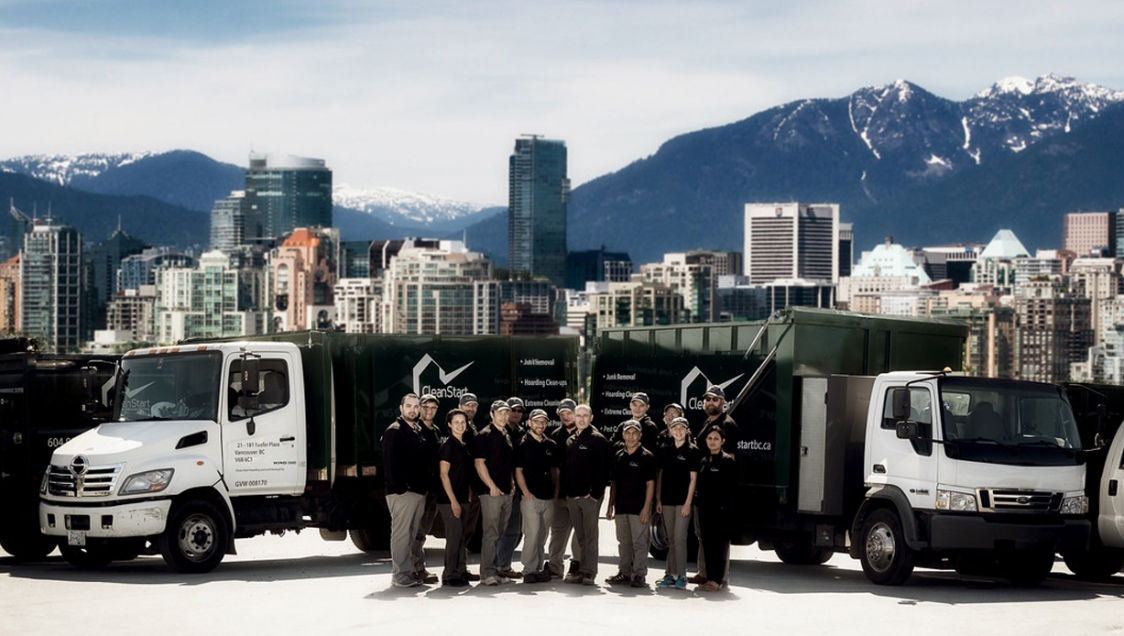 A group of diverse people in uniform, standing before trucks emblazoned with "Clean Start" against the city skyline