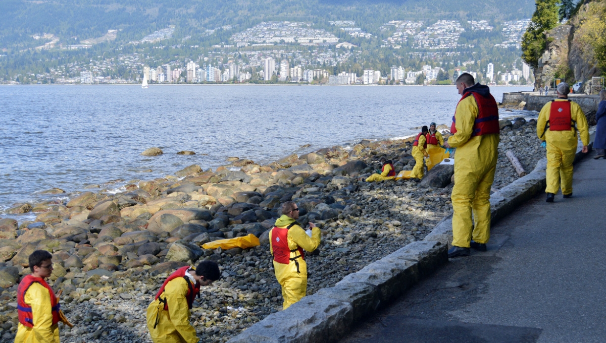 People in yellow protective gear and life jackets scour the rocky shore of a waterfront