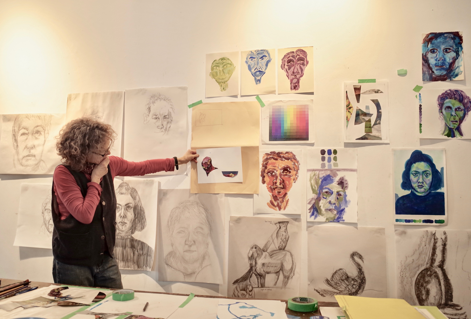 Person looking reflectively at a wall covered in charcoal drawings and watercolours