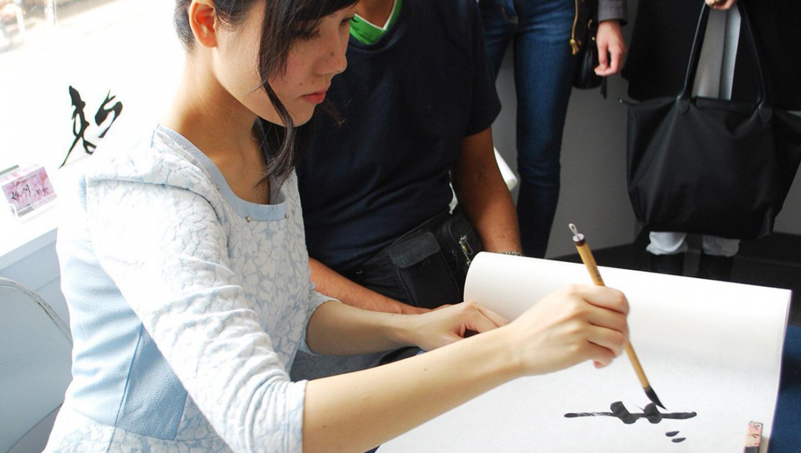 A yound dark haired woman holding a brush pen and practicing chinese calligraphy