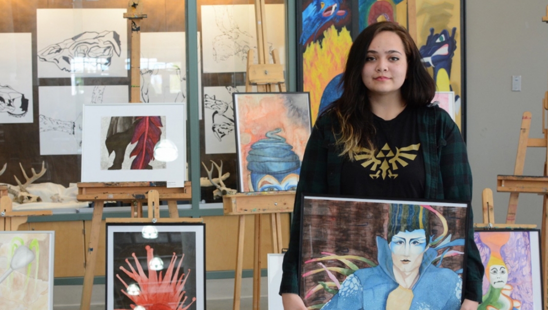 A young woman with dark hair posing with her paintings