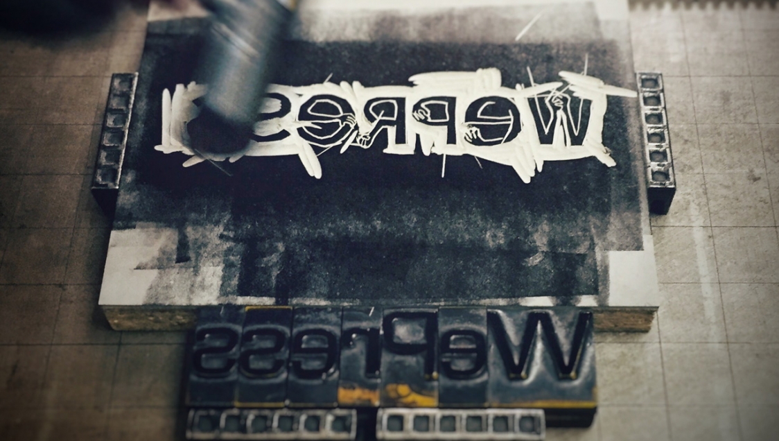 A writing press relief reading "WePress" in black and white, with the printing blocks mirrored underneath 