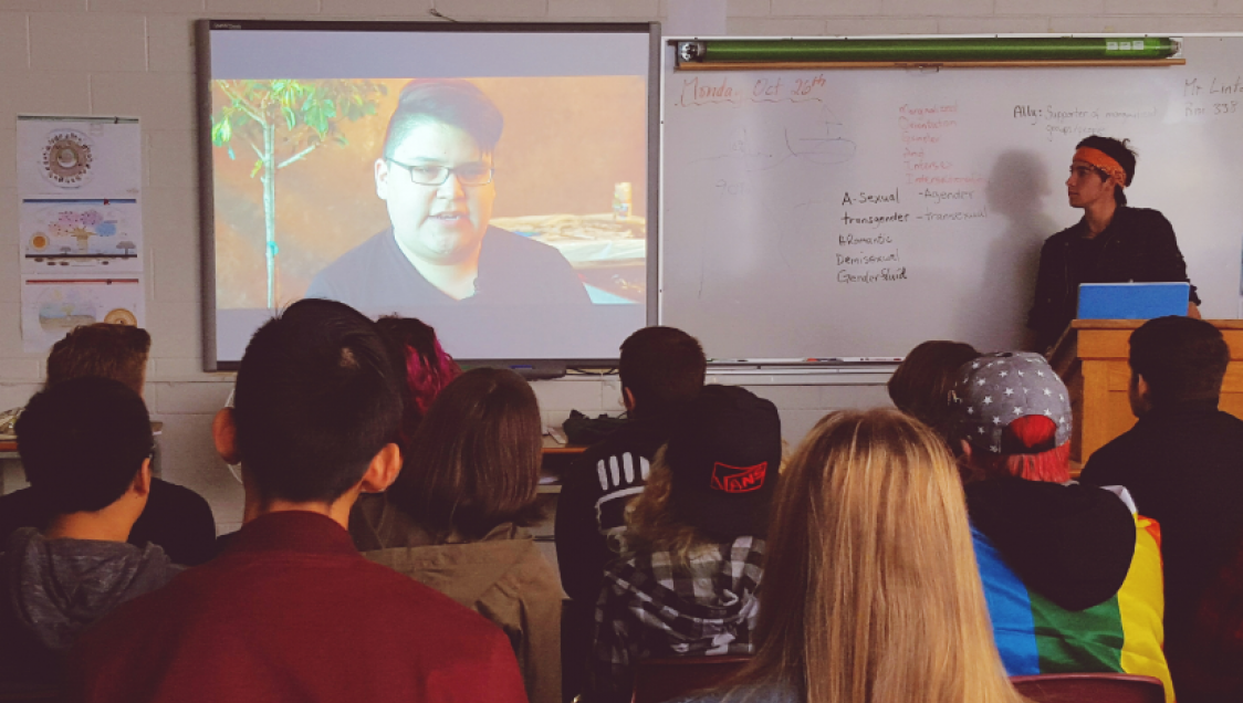 A student presenting a video in a dimly lit classroom to their peers