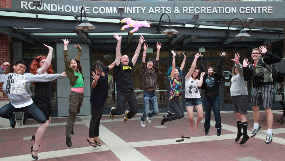 A diverse group of people in mid-jump in front of a community center