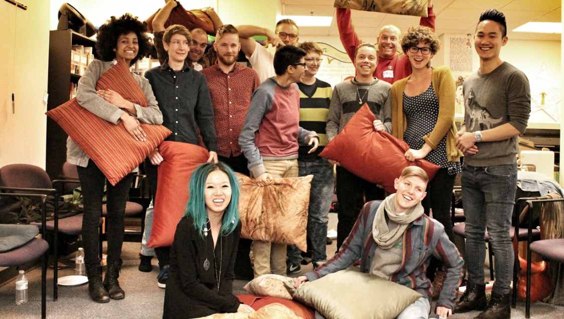 A group of smiling youth gathered together, holding pillows and cushions