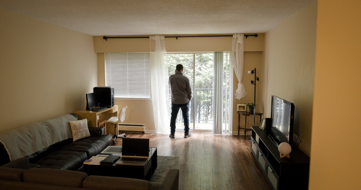 Posterior view of a man standing in his living room on his phone, looking out from the open patio doors