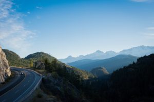 Lush, forested mountainside view of a car driving on a winding road 