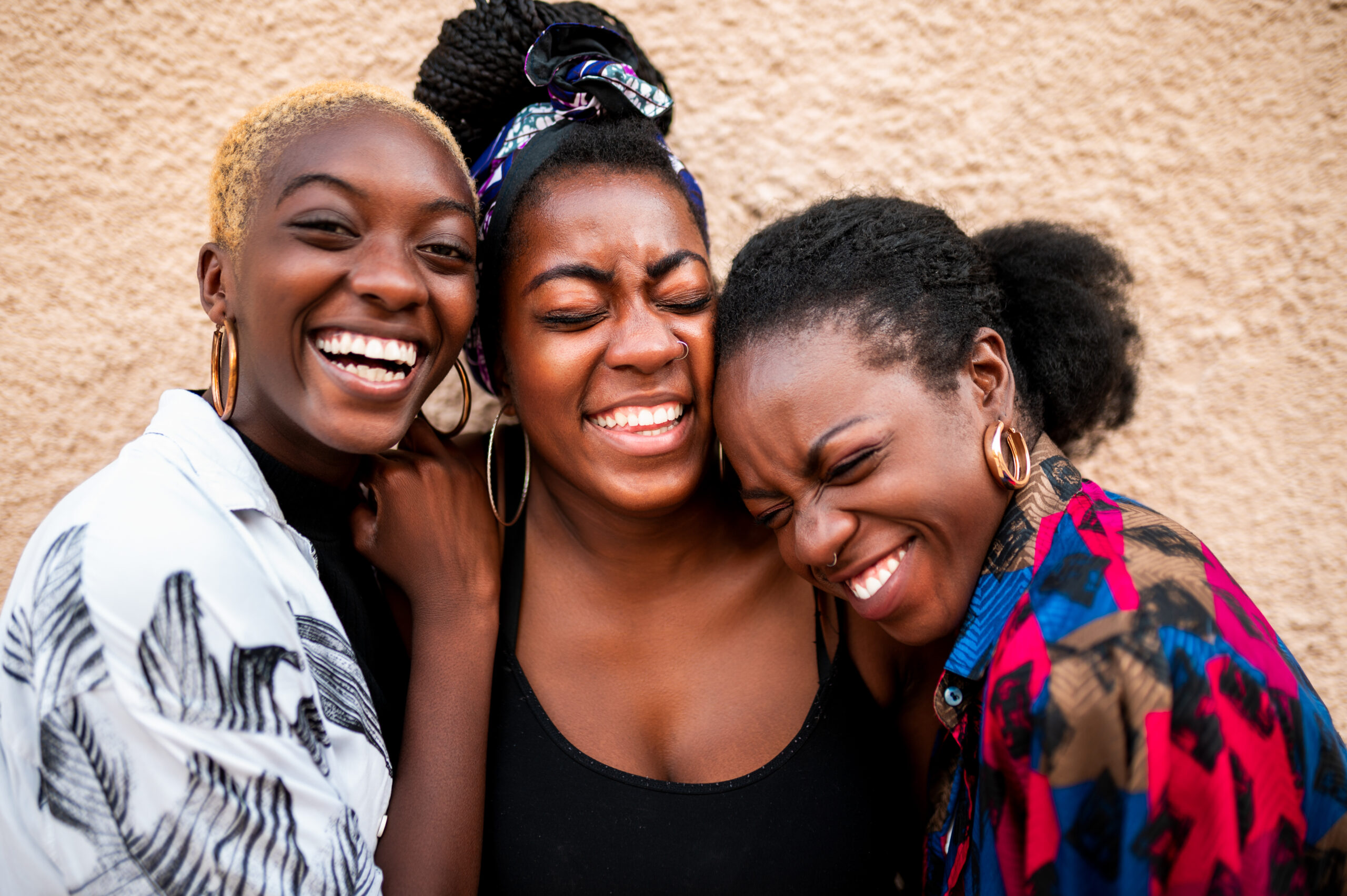 Three Black women smiling for the camera while embracing one another.