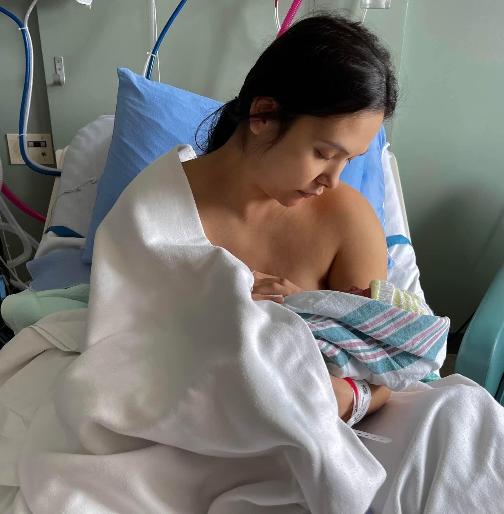 A Southeast Asian woman breastfeeding her newborn on a hospital bed.
