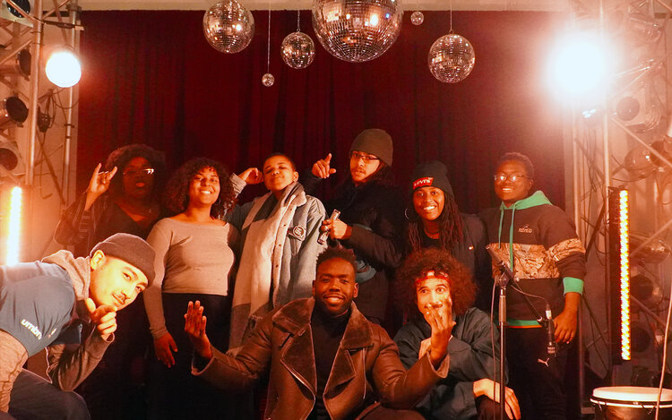 Group of BIPOC youth and young adults posing for the camera in a low lit room with disco balls reflecting the light.