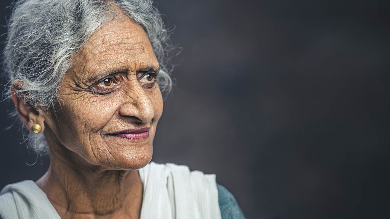 A confident older Indian woman with long grey hair wearing a sari.
