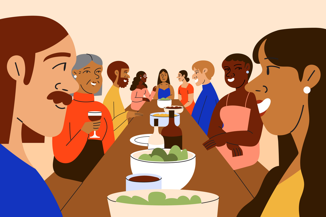 A multiracial group of people gather for a dinner party at a long shared table