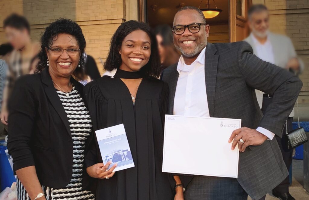 Three people are pictured together smiling. One of them is holding up a diploma.