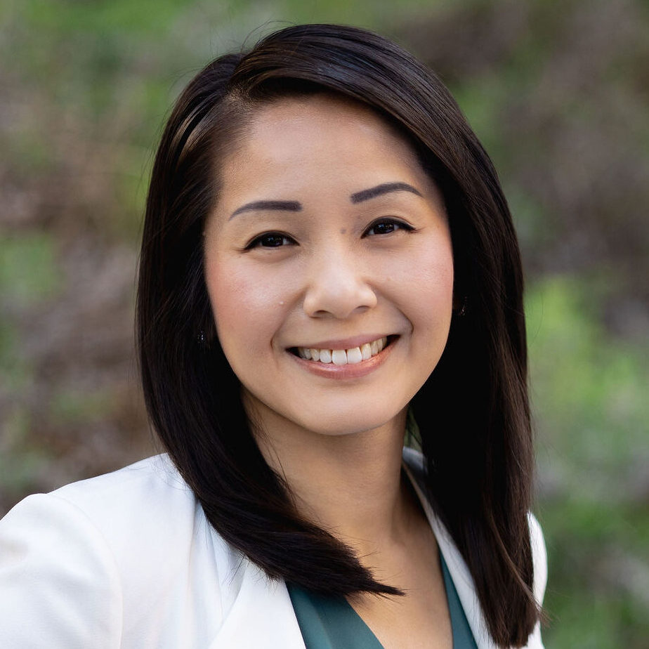 Headshot of Peggy Lam. She has mid-length black hair and is wearing a white blazer on top of a turquoise top.