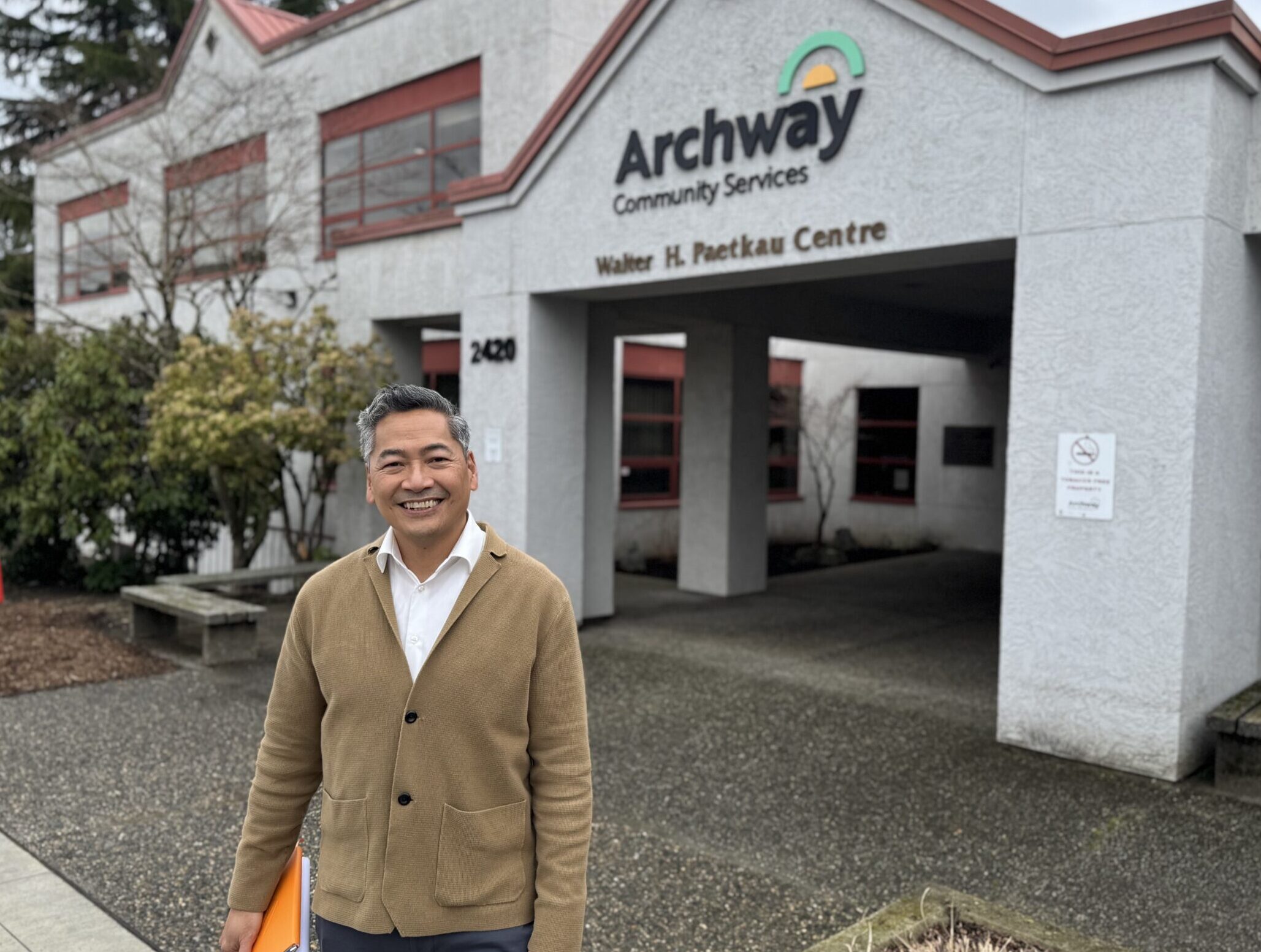 Rod archway 2 A person with short gray hair, wearing a yellow sweater is pictured smiling at the camera. He's standing in front of a building that says Archway.