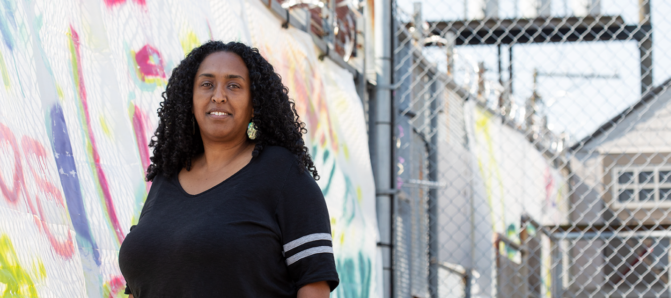 1 A smiling black woman in a black shirt standing near a colourful wall mural