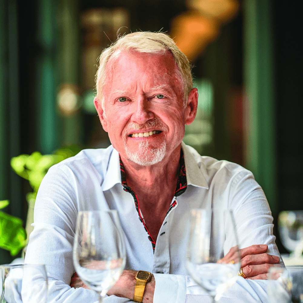 Smiling older man in a white collared shirt sitting with arms crossed at a table