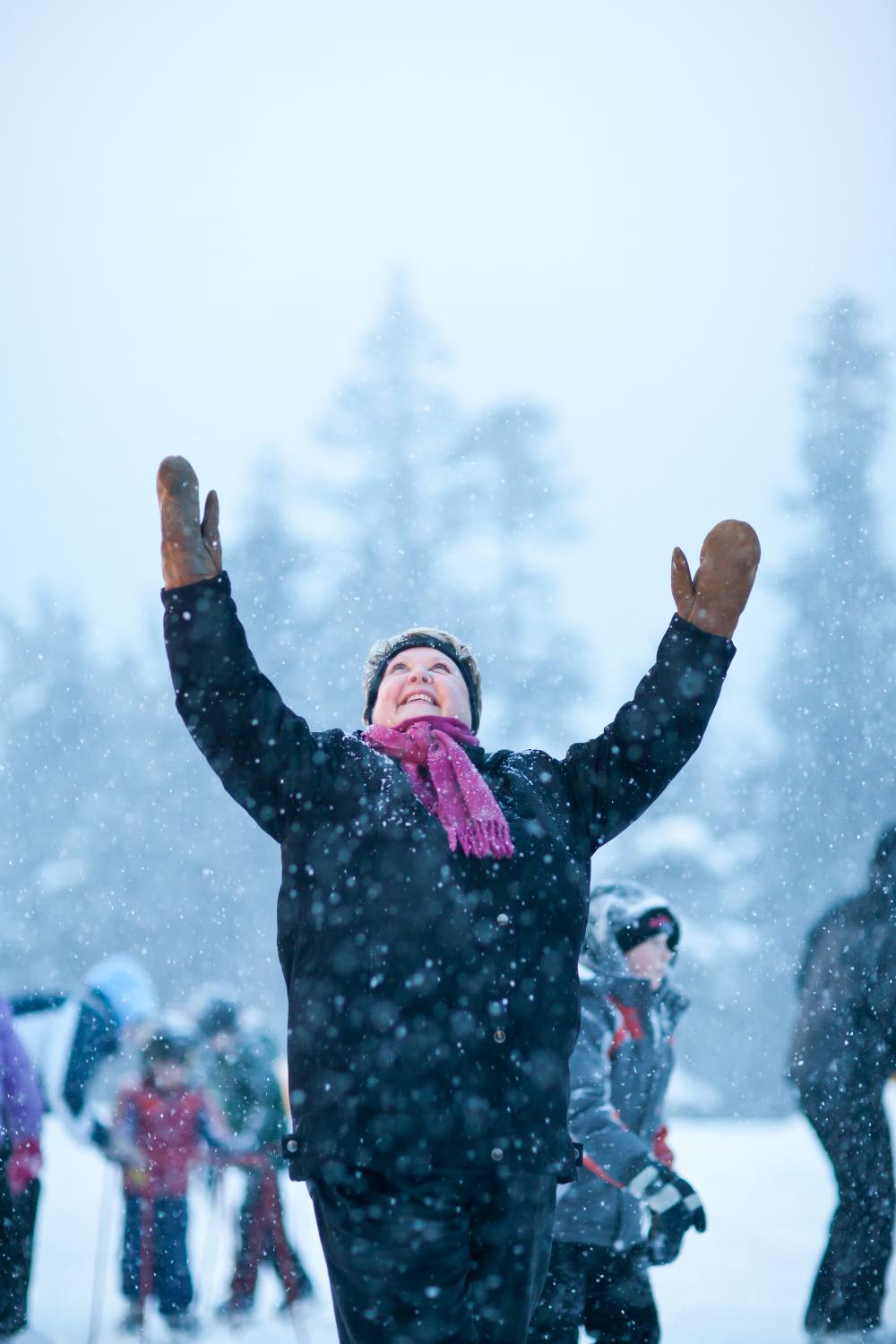Happy smiling woman in winter wear, raising her arms up at the sky as snow falls