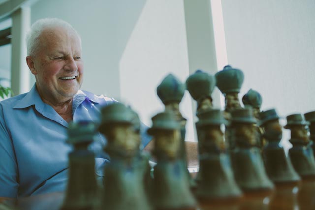 An elderly man smiling in front of a chessboard
