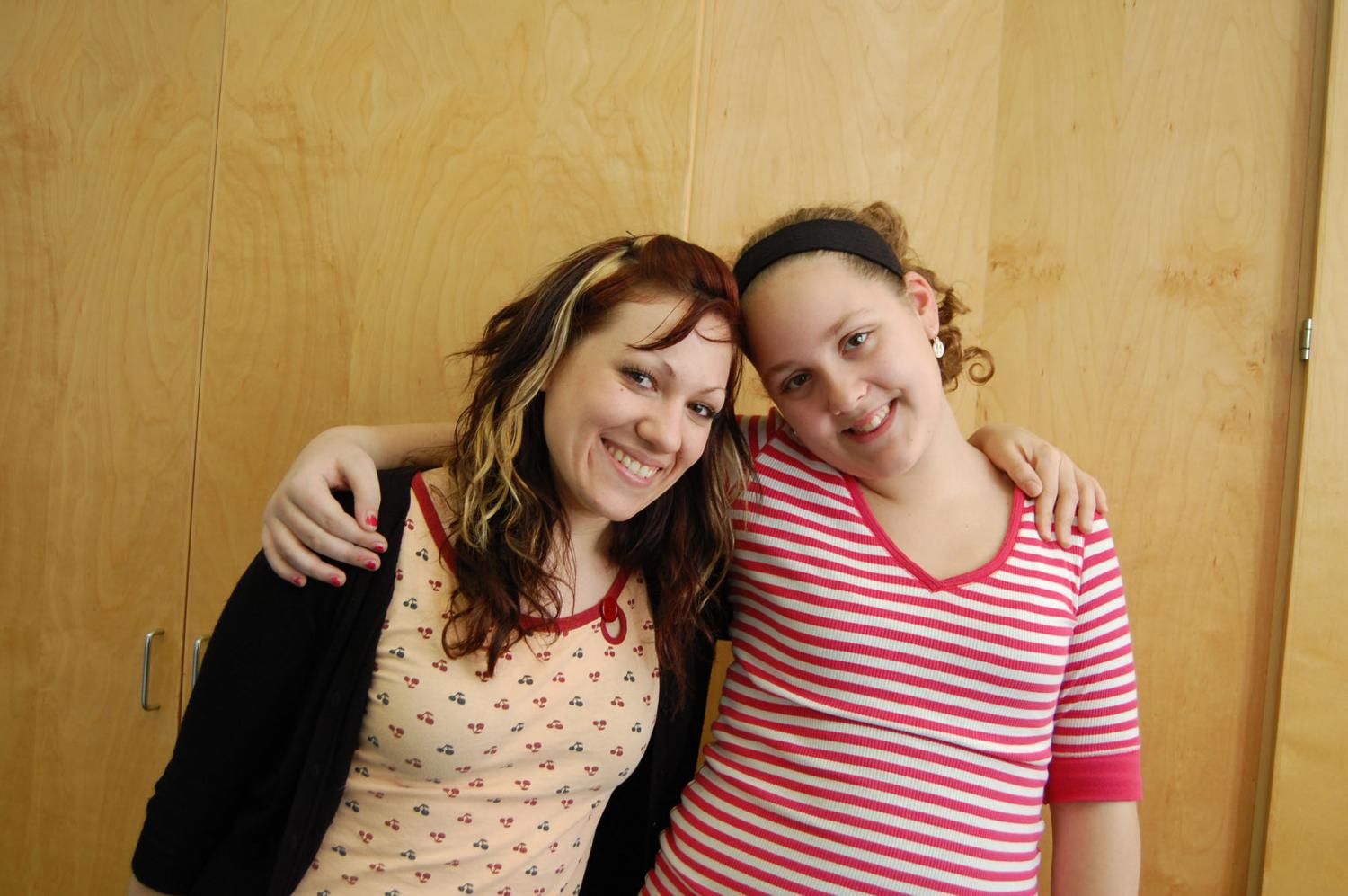 Two young women standing side by side, arms around each others shoulders, smiling