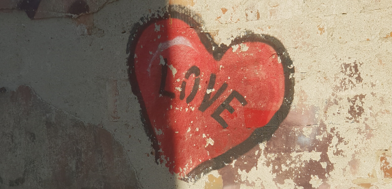 Red spray-paint heart on a concrete wall, outlined in block, with the word "Love" written in the middle in black