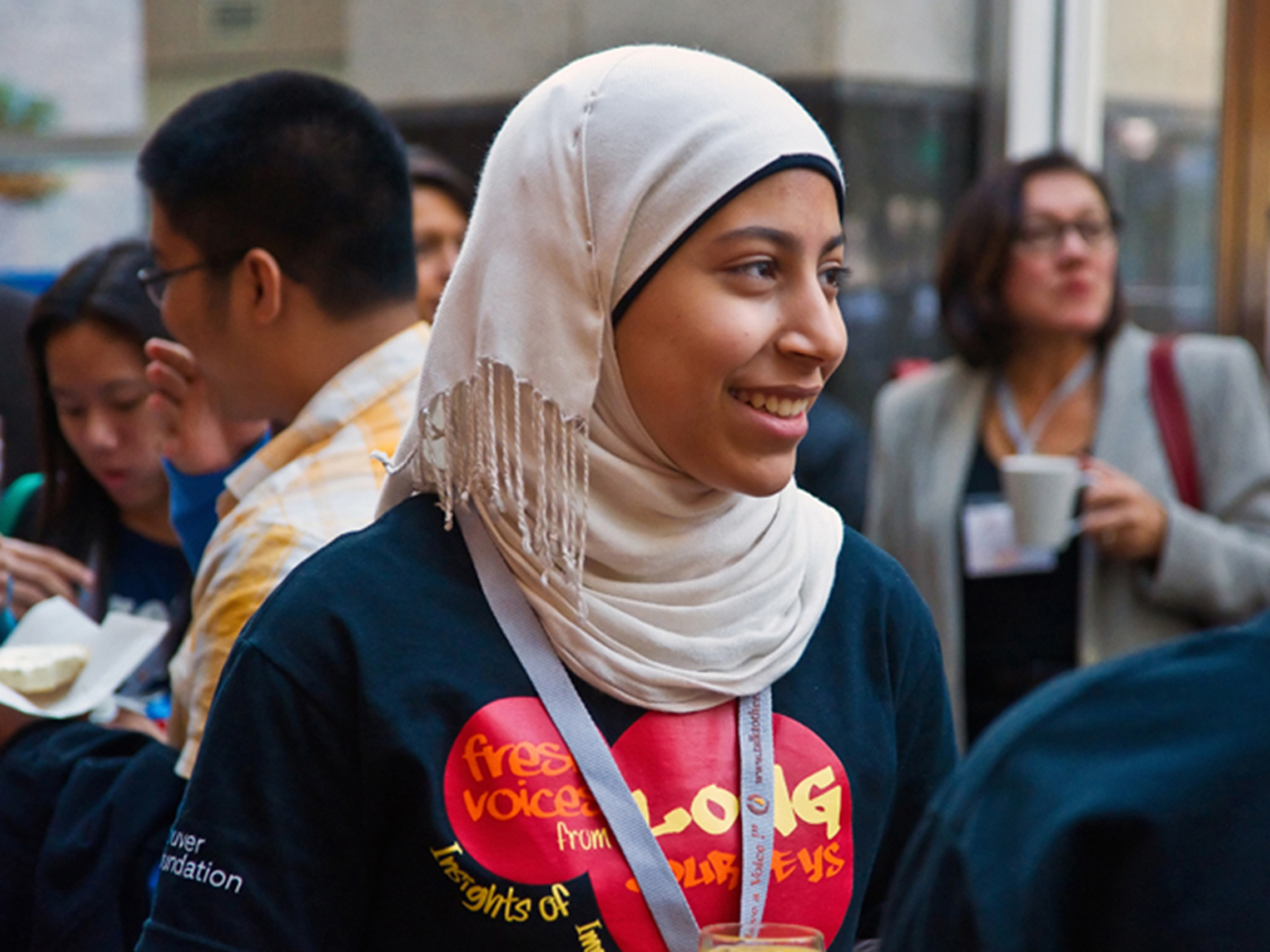 A young woman of colour in a navy Vancouver Foundation shirt and cream coloured Hijab, smiling