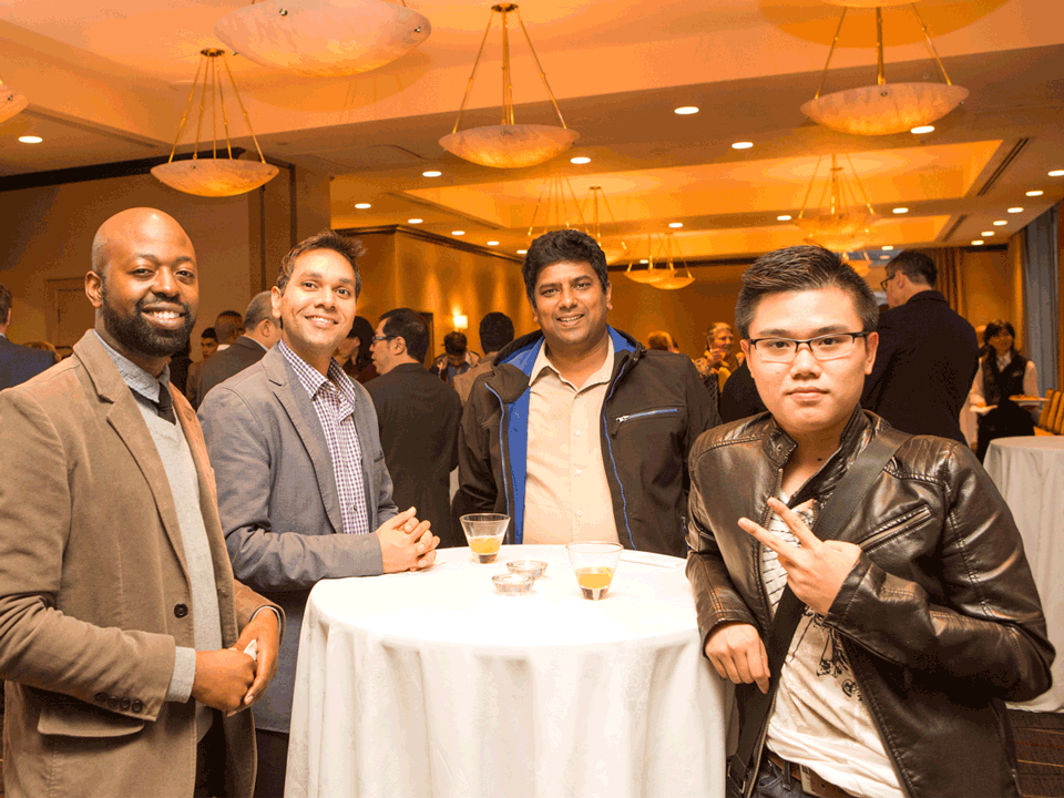 4 men of colour standing around a raised bar table and smiling, with the closest man flashing a peace sign with his index and middle fingers