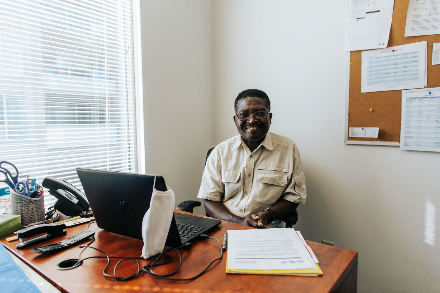 A smiling black man sitting at his desk with a laptop 